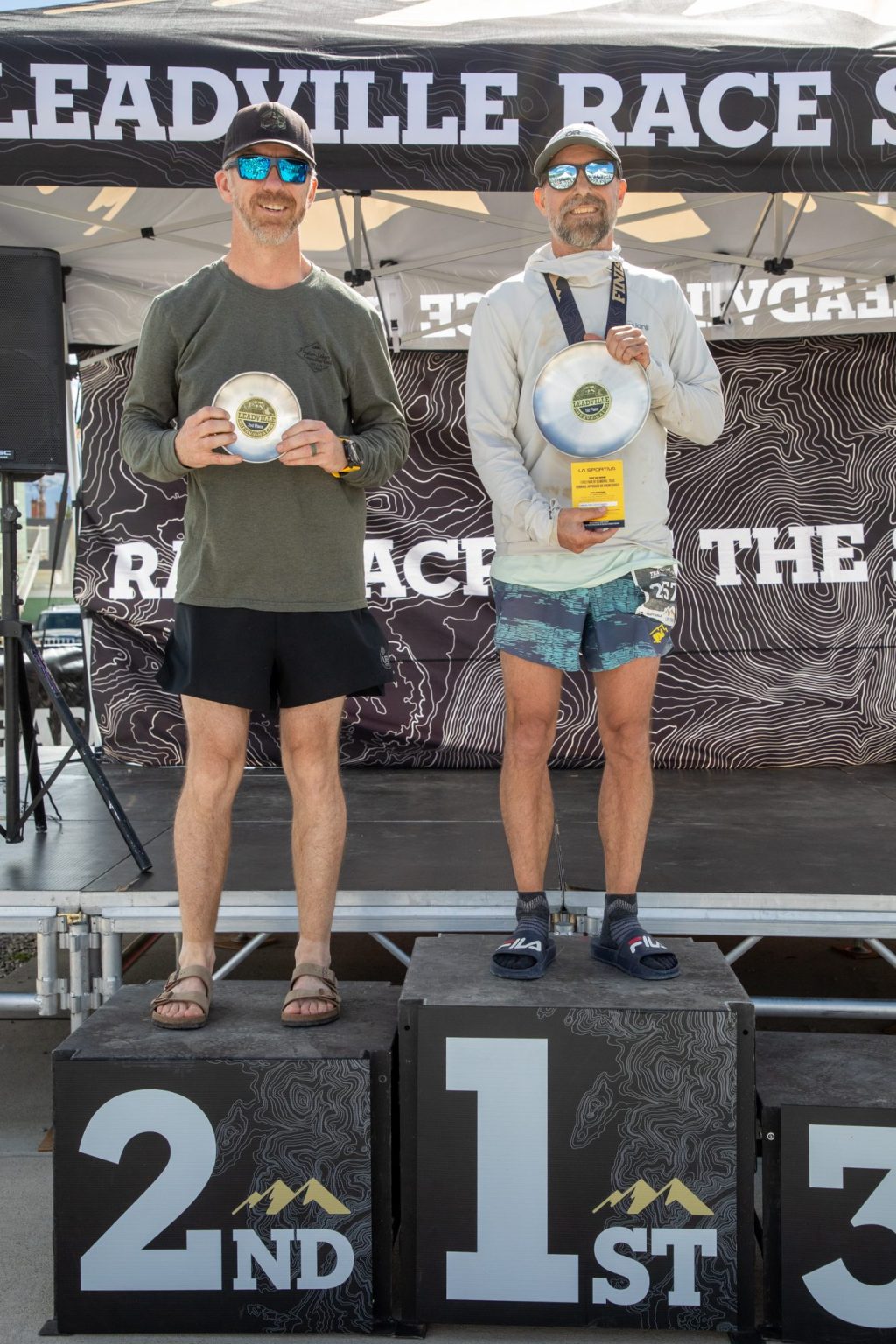 Dr. Brian Schulz on the first-place podium at the Leadville Heavy Half, holding his age-group award